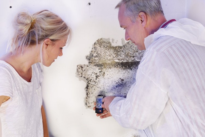 Een vochtexpert toont aan een jonge vrouw dat er vocht in huis is door het vochtgehalte van een muur te meten