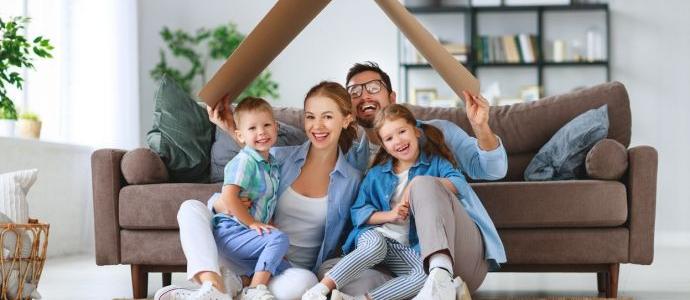 Une famille heureuse est assise par terre devant le canapé dans leur maison sans humidité avec un toit en carton au-dessus de leur tête