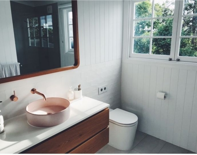 Witte badkamer met roze lavabo en donkerbruine accenten.
